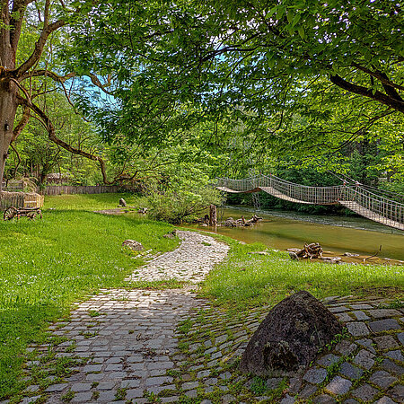 [Translate to English:] Die Hängebrücke im Mühlendorf liegt idyllisch im Grünen.