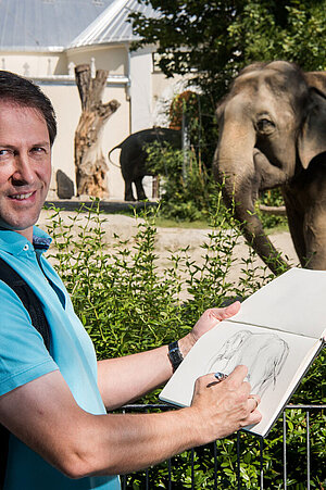 Der Leiter des Zeichenkurses beim Anfertigen einer Skizze, im Hintergrund sieht man das Fotomodell, den Elefanten.