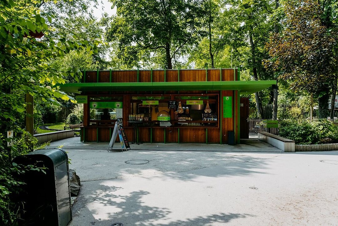 Der Kiosk Kinderland aus der Ferne. Ein grünes Vordach und zahlreiche Süßigkeiten sind zusehen.