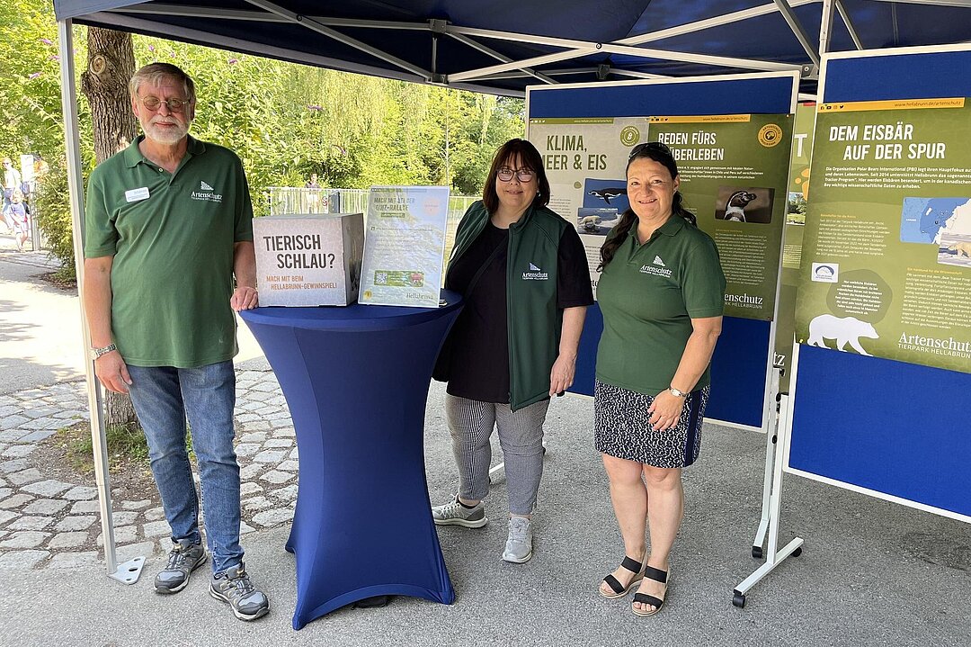 Drei Mitarbeiter*innen stehen am Infostand bei der Einwurfbox für die Quizrallyes.