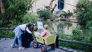 Drei Kinder sowie eine Mutter beobachten die Kattas, zwei Kinder sitzen in einem grünen Bollerwagen.